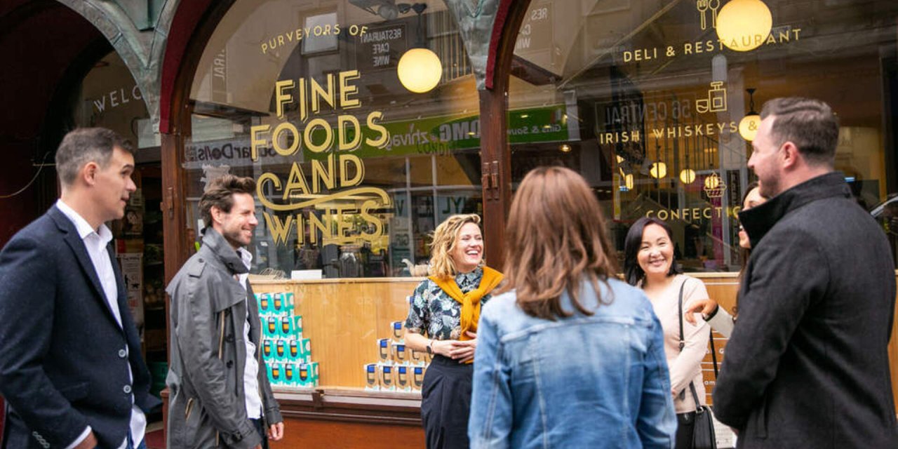 Woman with yellow jumper standing outside of a shop with brown exterior with people wearing black jackets