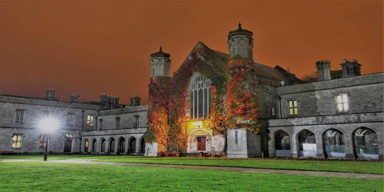 Orange sky with grey bricked old tall building covered in fall leaves, behind bright green grass